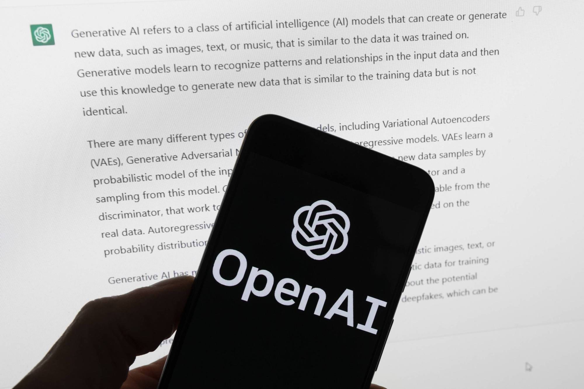 نشان OpenAI روی تلفن همراه در مقابل صفحه رایانه‌ای که خروجی ChatGPT را نمایش می‌دهد