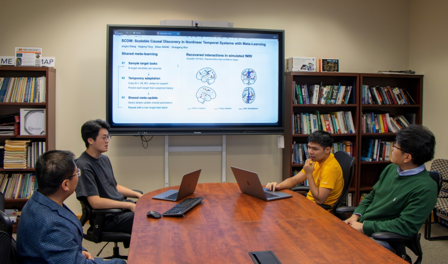 Four UTC computer science researchers meet around a conference table while a screen displays visuals from their NeurIPS-accepted paper on scalable causal discovery.