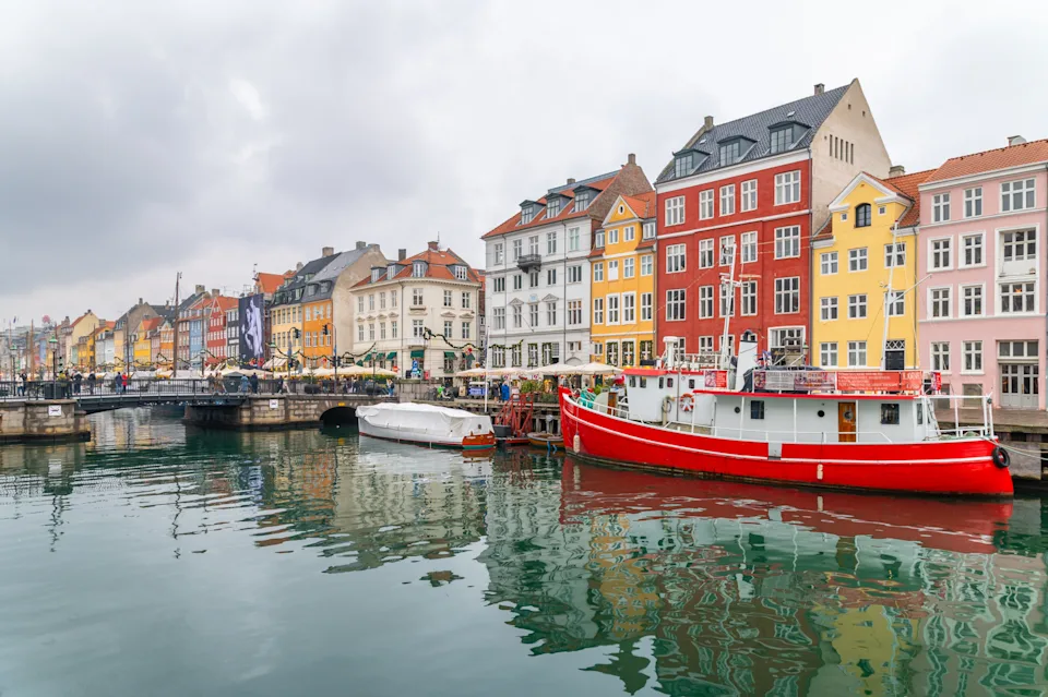 Colorful buildings and boats line the canal in a scenic view of Nyhavn, Copenhagen, under an overcast sky