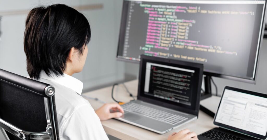 IT professional reviewing code and system settings across multiple screens at a workstation