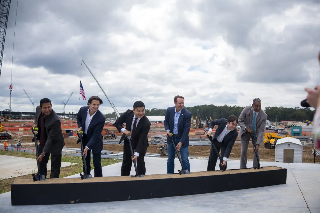 Santanu Biswas, Giordano Albertazzi, Asher Genoot, Governor Jeff Landry, James Bradbury, and Bob Pragada participate in a groundbreaking ceremony for an AI data center campus.