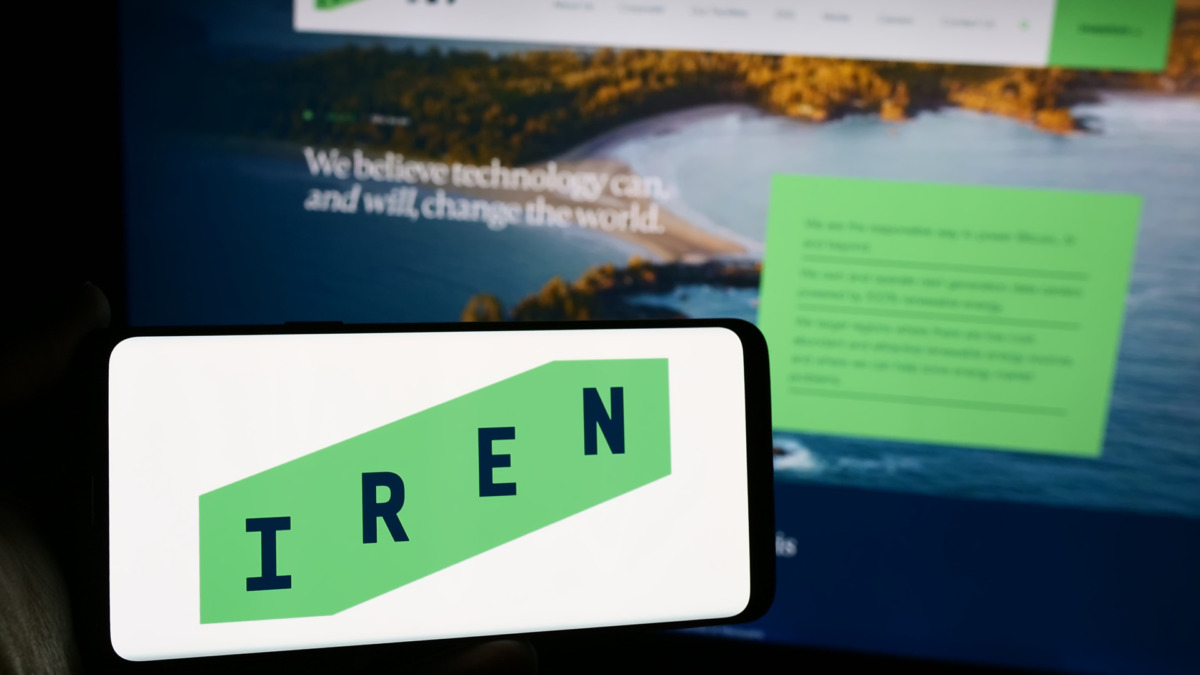 نمایش لوگوی شرکت استخراج بیت‌کوین استرالیایی Iris Energy Ltd. (IREN) روی تلفن همراه در مقابل یک صفحه وب