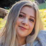 A woman wearing a jacket sits in a park.