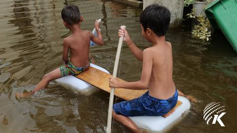 Children sit on plastic containers topped with a wooden board, using a wooden stick to paddle through floodwaters in a community in Prek Pra district, Phnom Penh. Kiripost/Keng Sotherng
