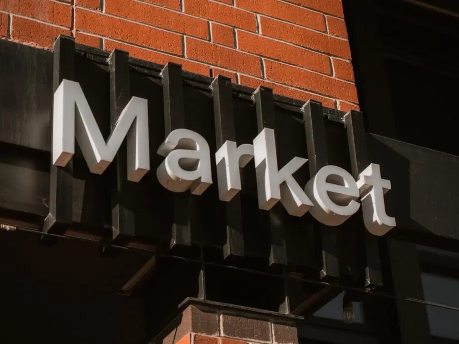 A sign with the word Market is mounted on a black frame against a red brick wall.