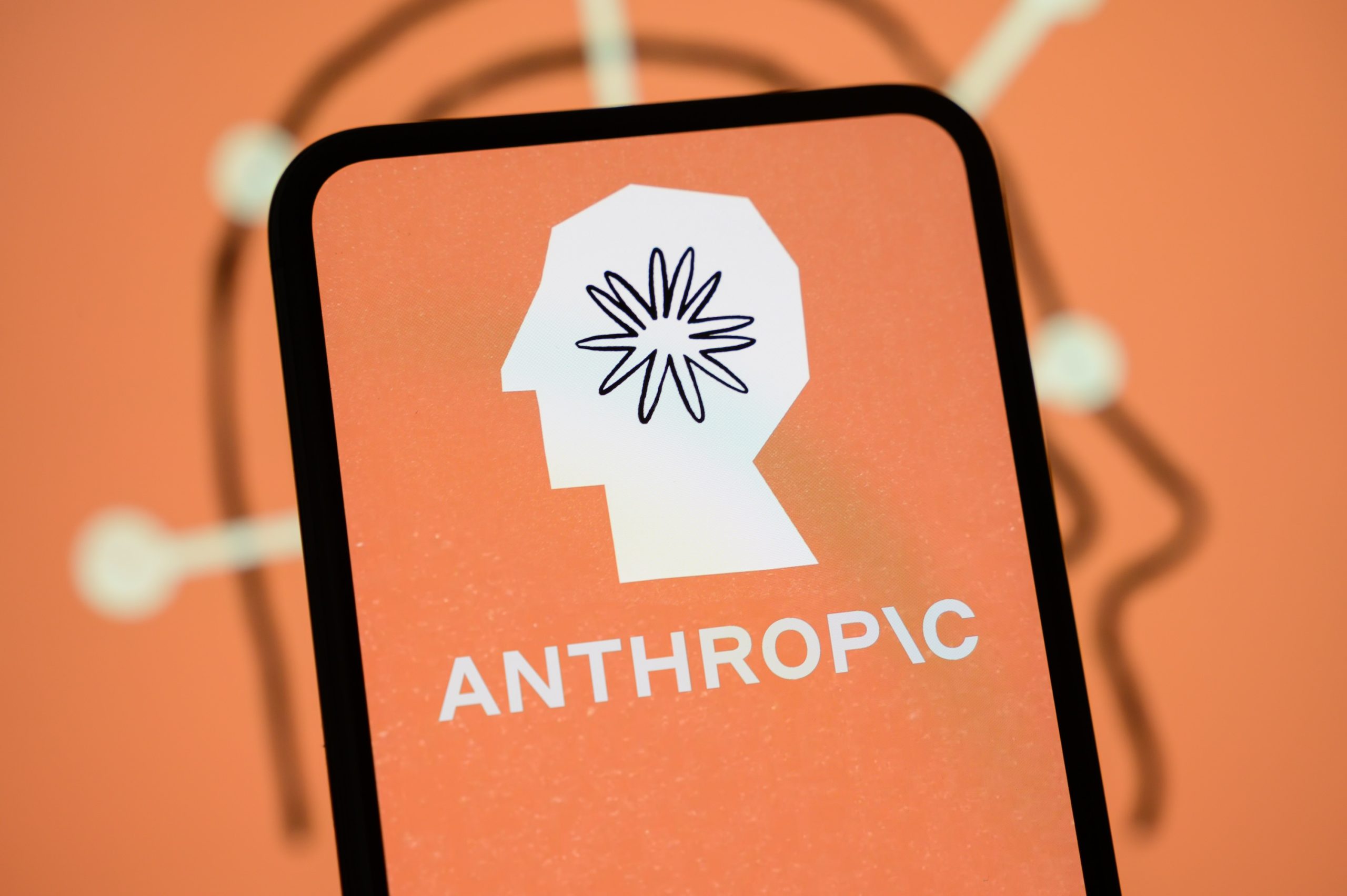 The Anthropic logo is displayed on the screen of a smartphone with the company's branding in the background.