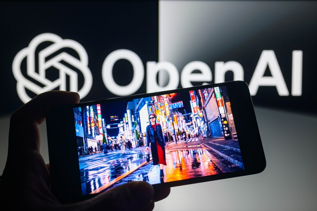 دستی که تلفن هوشمندی با نمایش مدل تبدیل متن به ویدئوی Sora در دست دارد و نشان OpenAI در پس‌زمینه دیده می‌شود